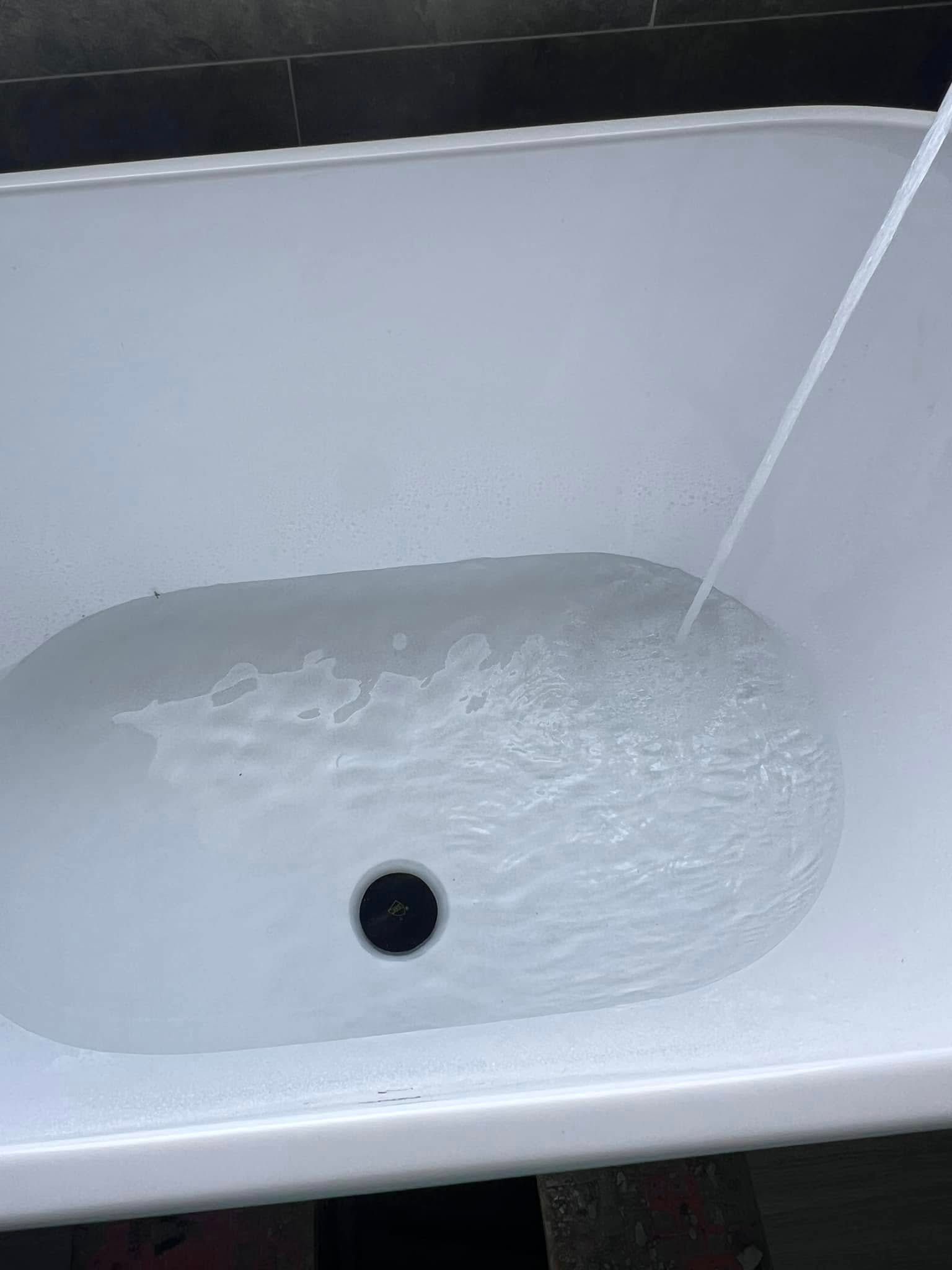 Water running into a white bathtub, filling around the drain.