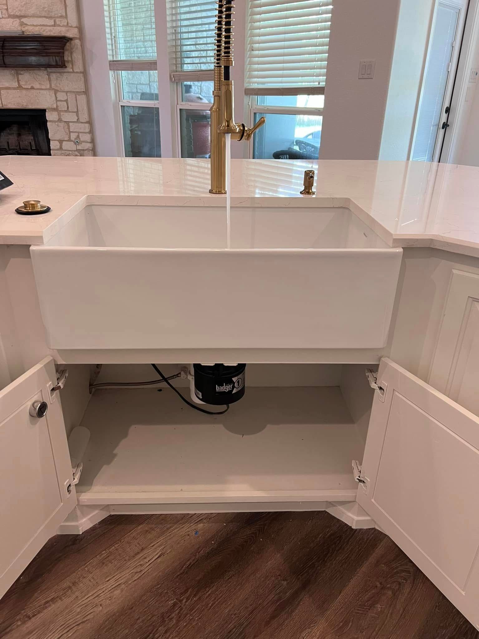 White farmhouse sink cabinet with open doors in a bright kitchen, showing plumbing and storage space underneath