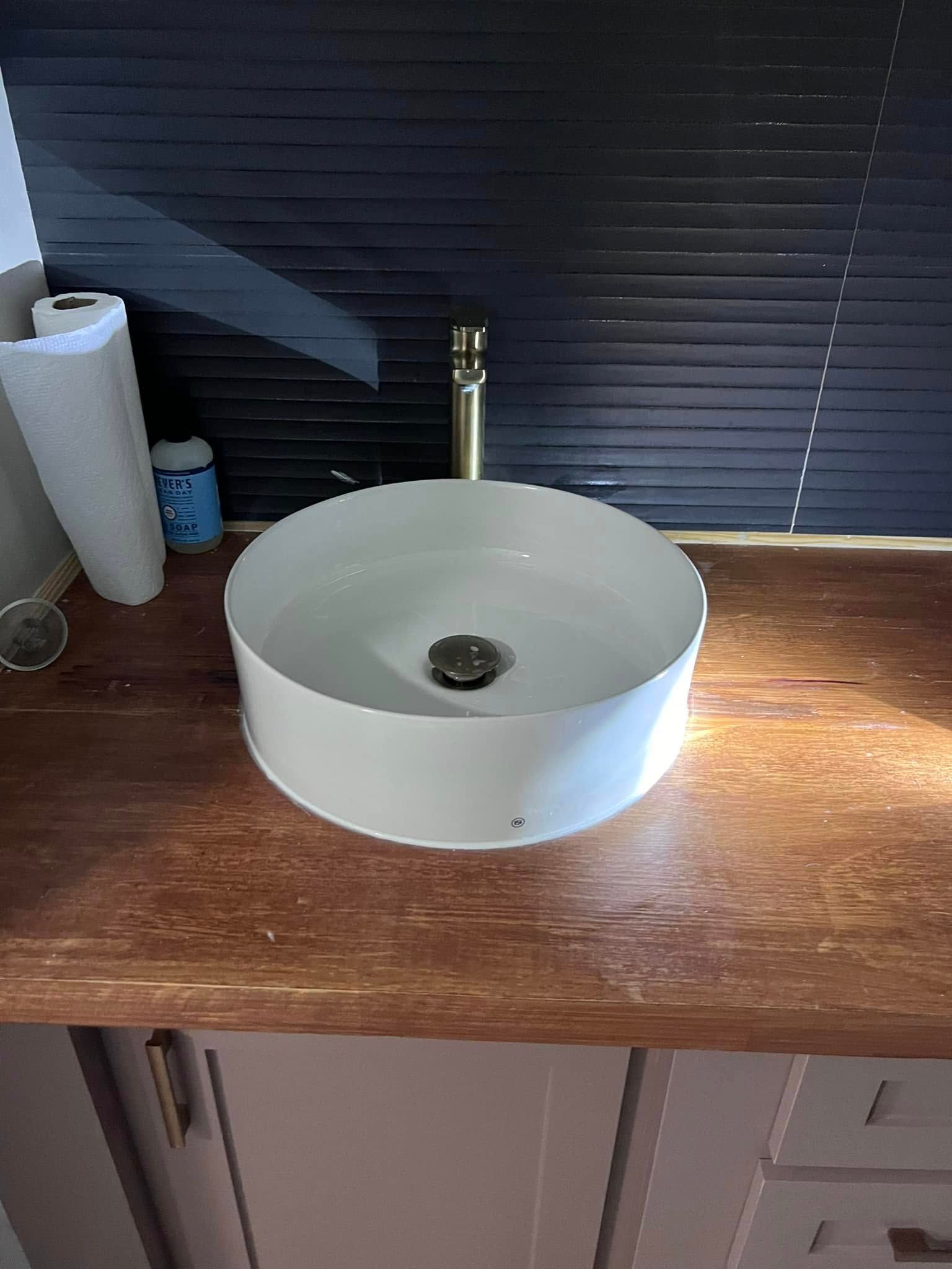 White vessel sink on a wooden countertop with a chrome faucet and dark blinds behind it
