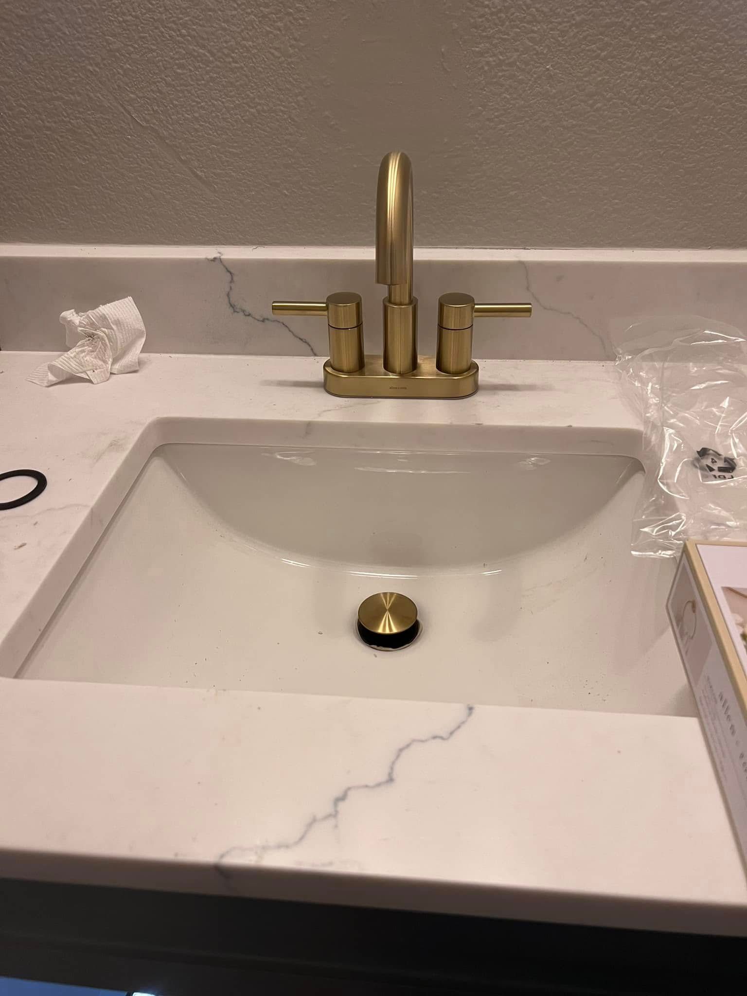 Bathroom sink with white countertop, gold faucet, and a small bottle on the left edge.