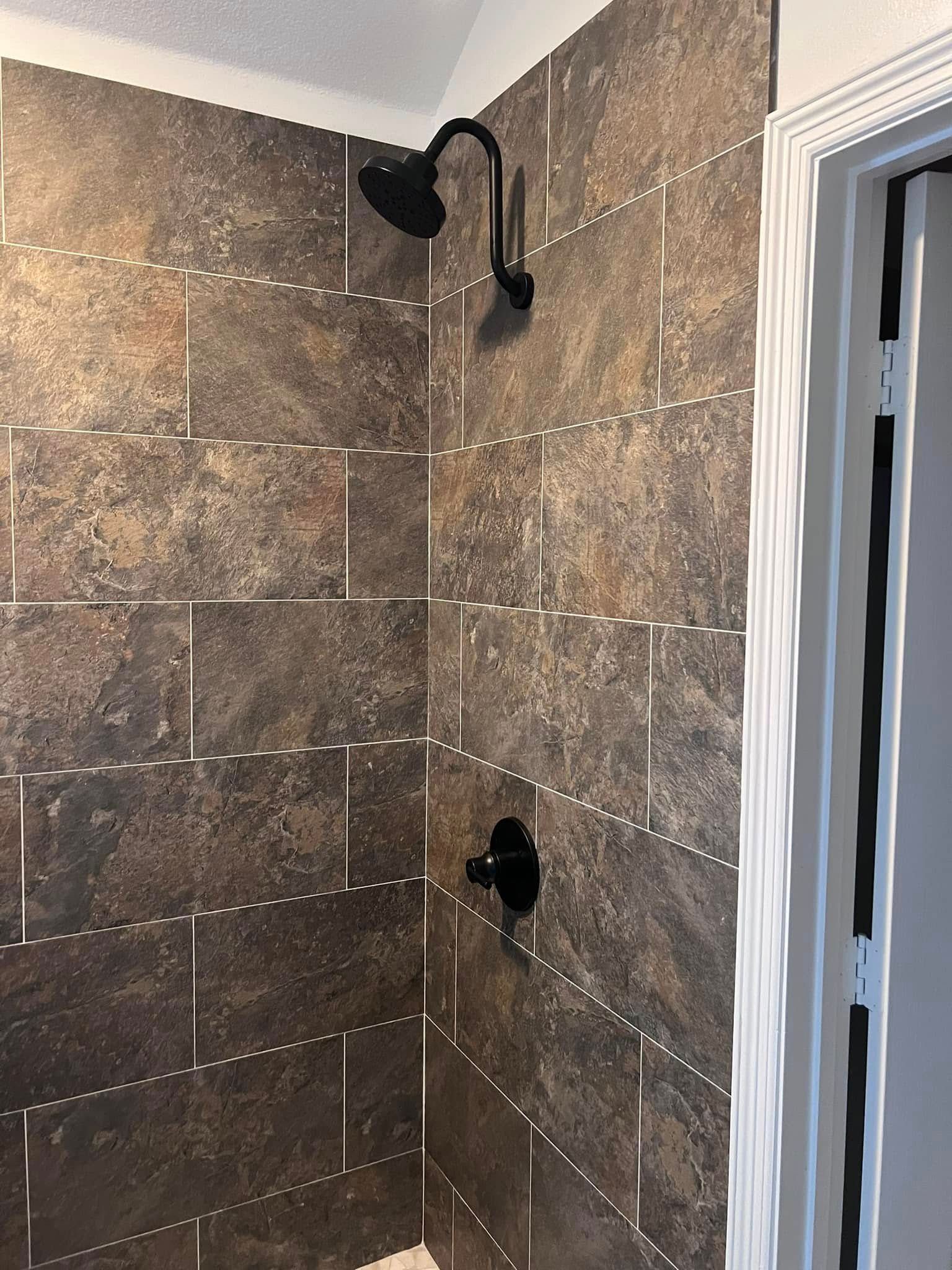 Tiled bathroom shower with black showerhead and fixture against brown stone walls.