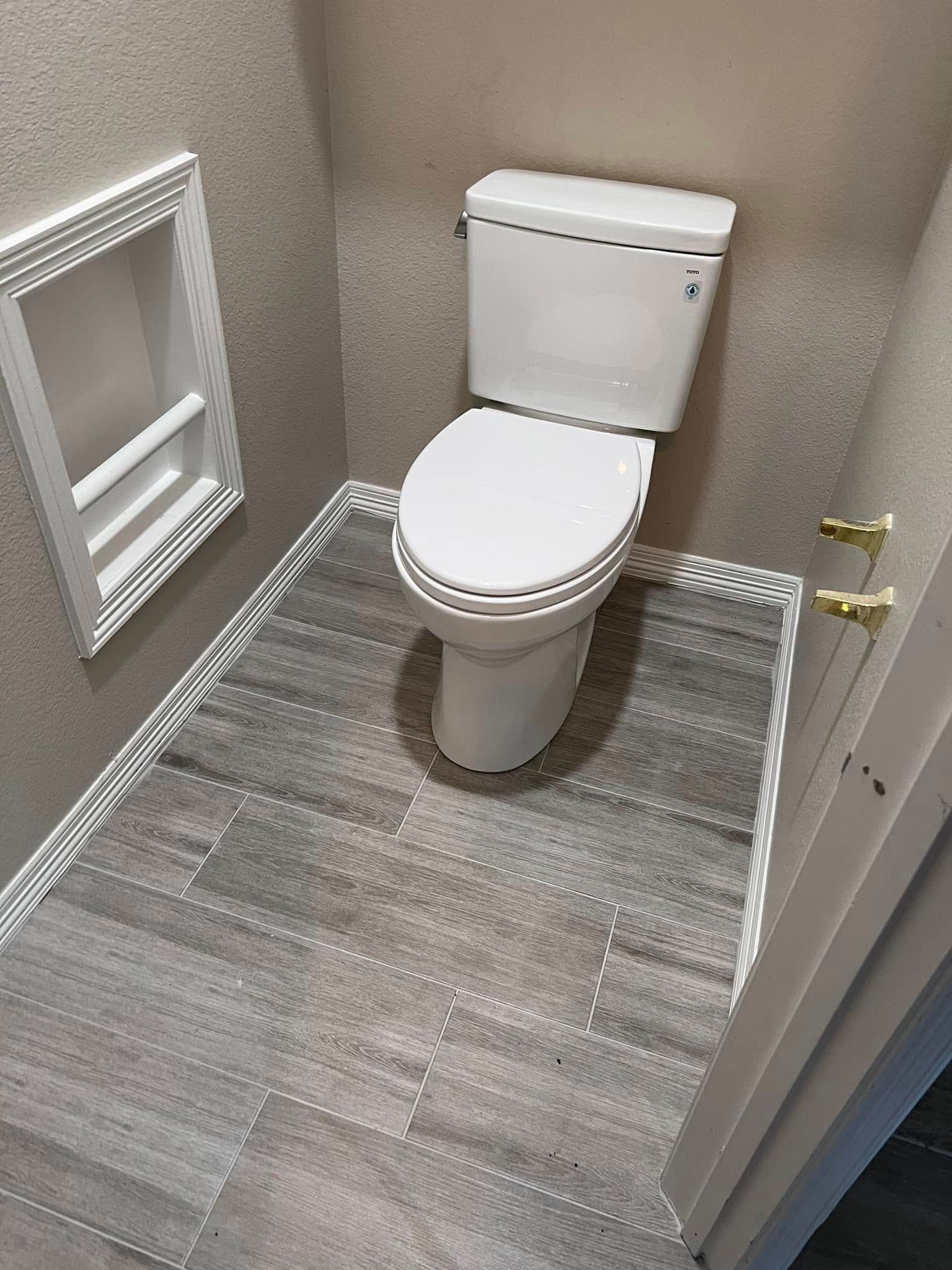 Small bathroom with a white toilet, gray wood-look floor, textured walls, and a wall-mounted mirror cabinet.