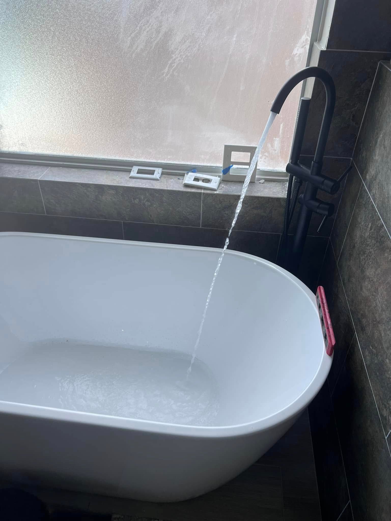 White bathtub beneath a window with water running from the faucet into the tub