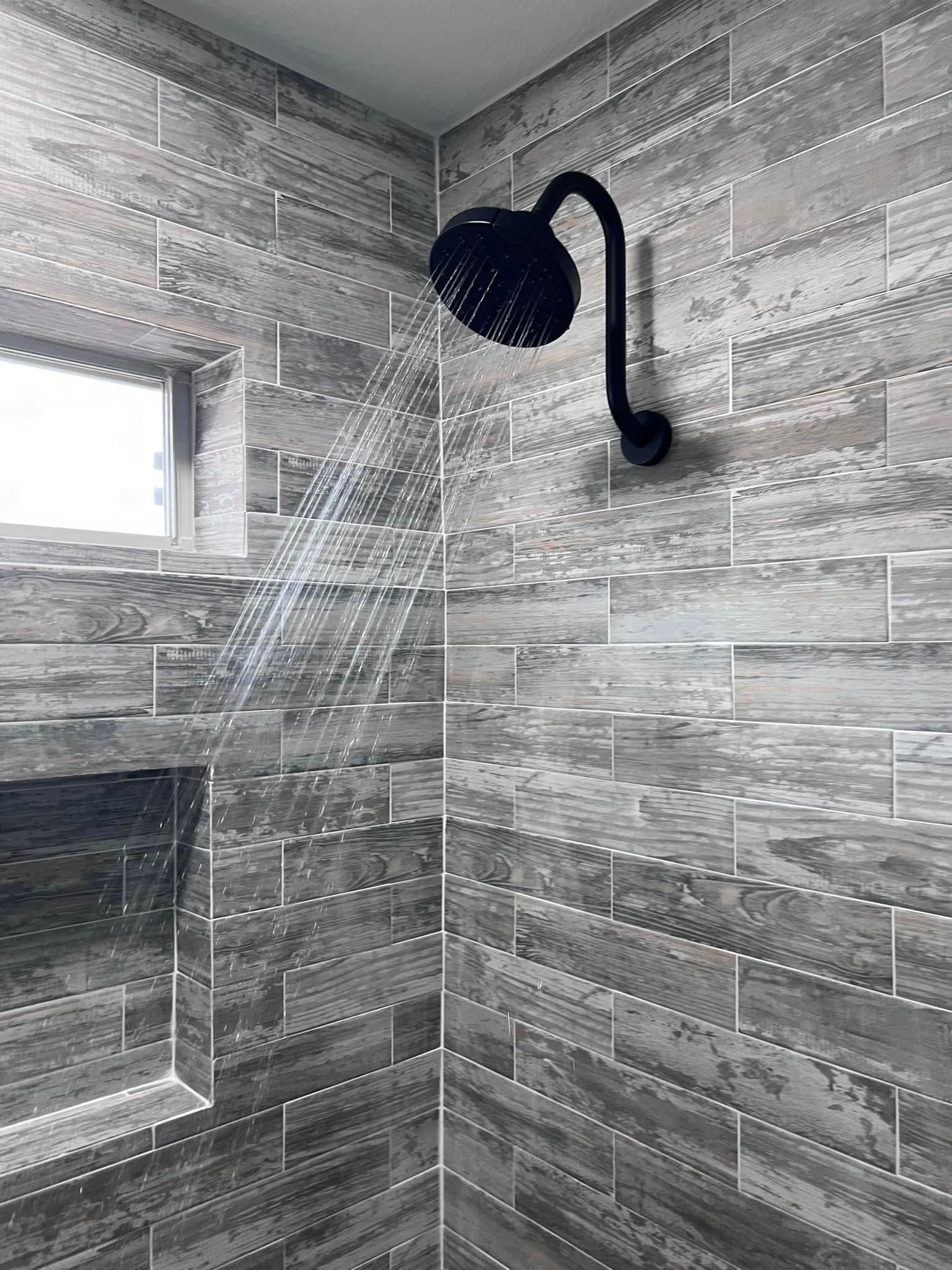 Gray tiled shower with black rainfall showerhead and water spraying onto the wall
