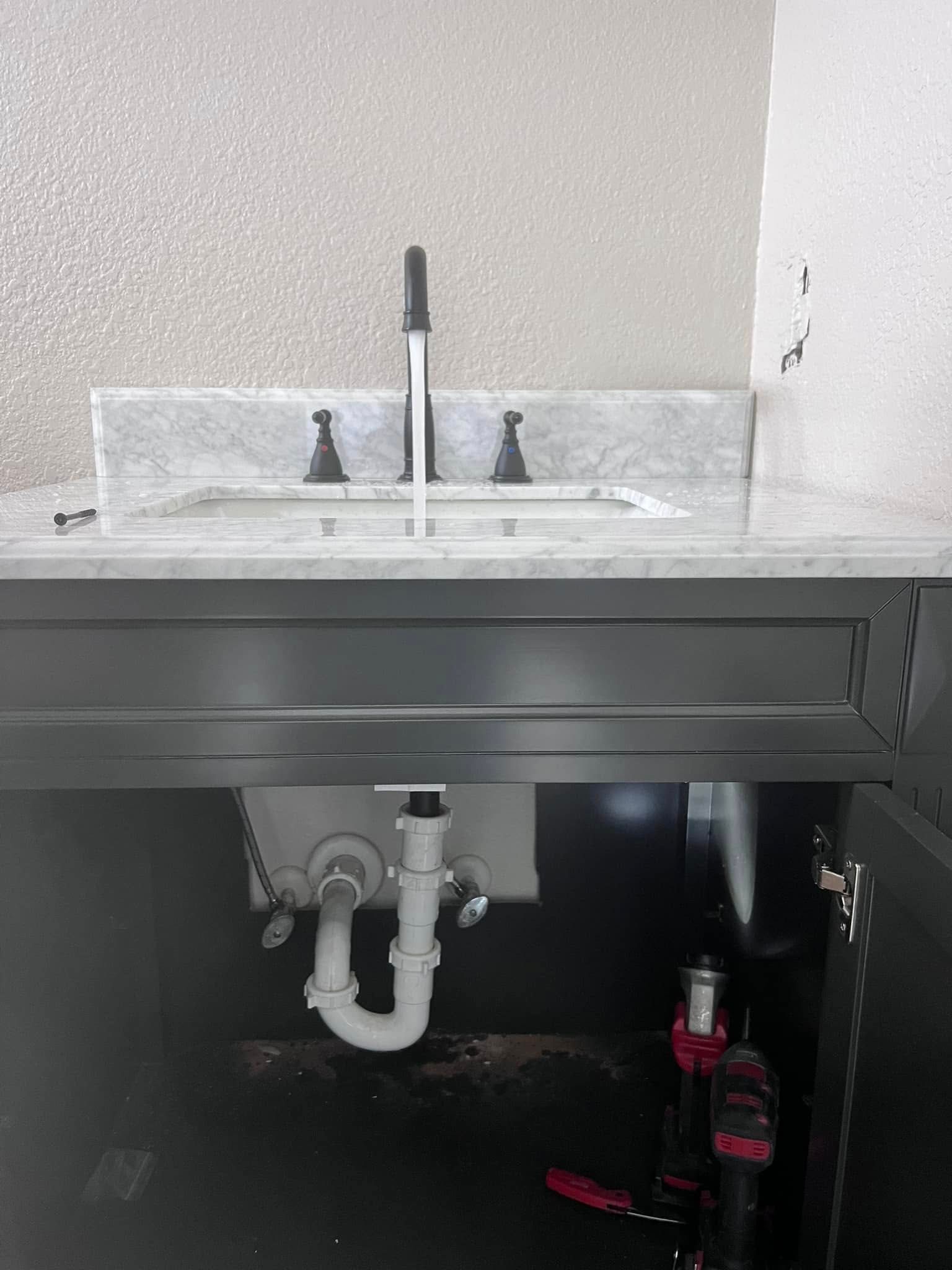 Bathroom sink under a gray countertop with exposed white drain pipes and cleaning supplies below