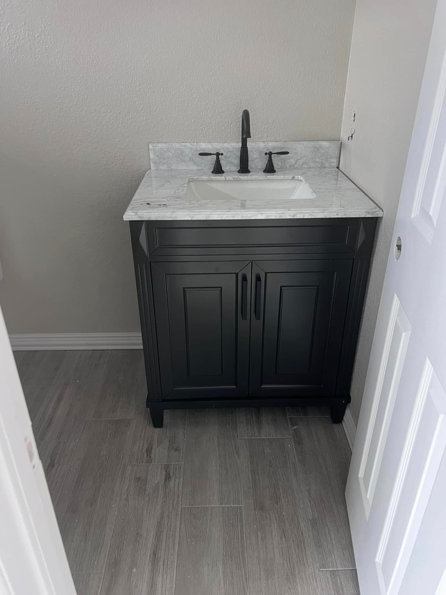 Small black bathroom vanity with marble sink top and mirror in a narrow room