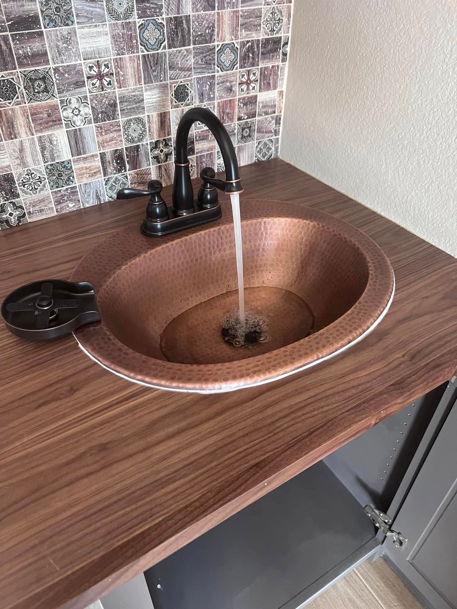 Copper sink with running faucet on a brown countertop in a small kitchen or bathroom area