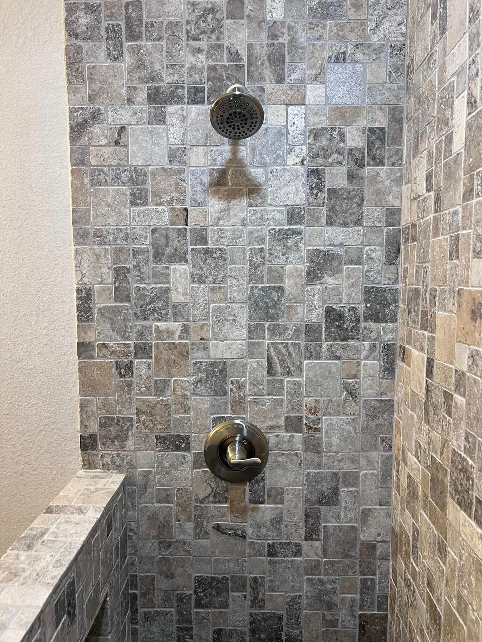 Tile shower wall with a black showerhead and a brushed metal control valve.