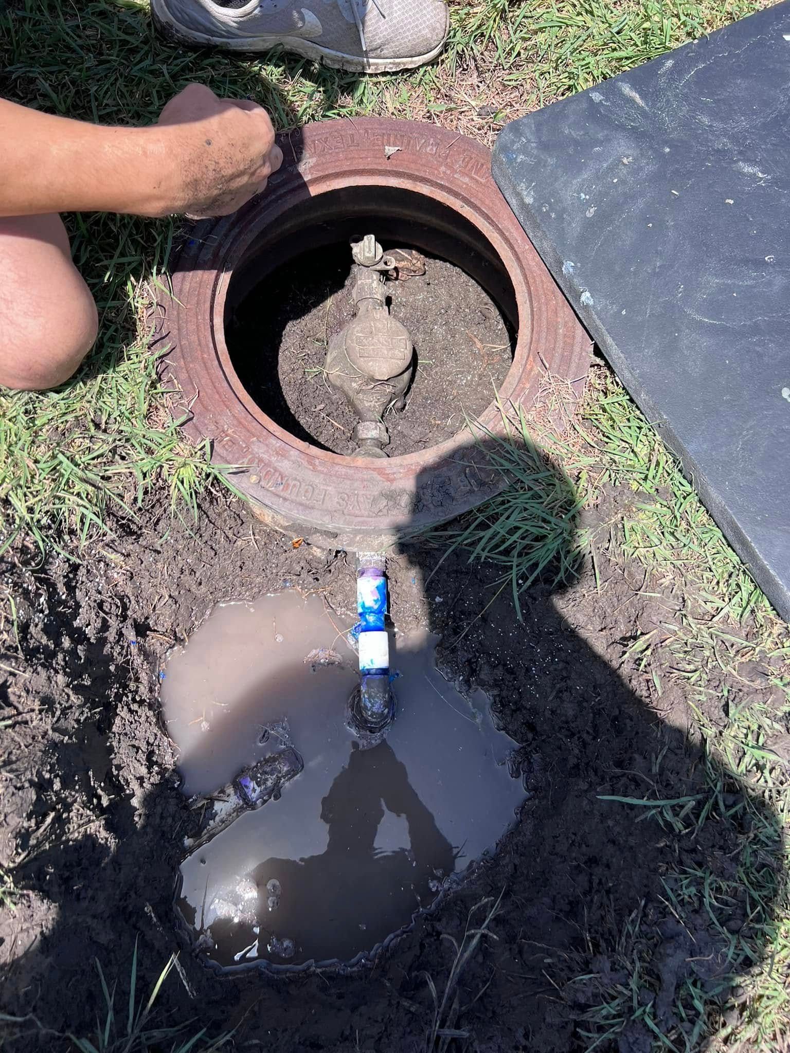 Open utility well with muddy water beside a grass edge and a blue bottle