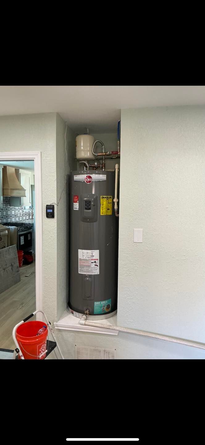 Utility closet with a gray water heater beside a doorway, bucket on the floor, and wall damage nearby