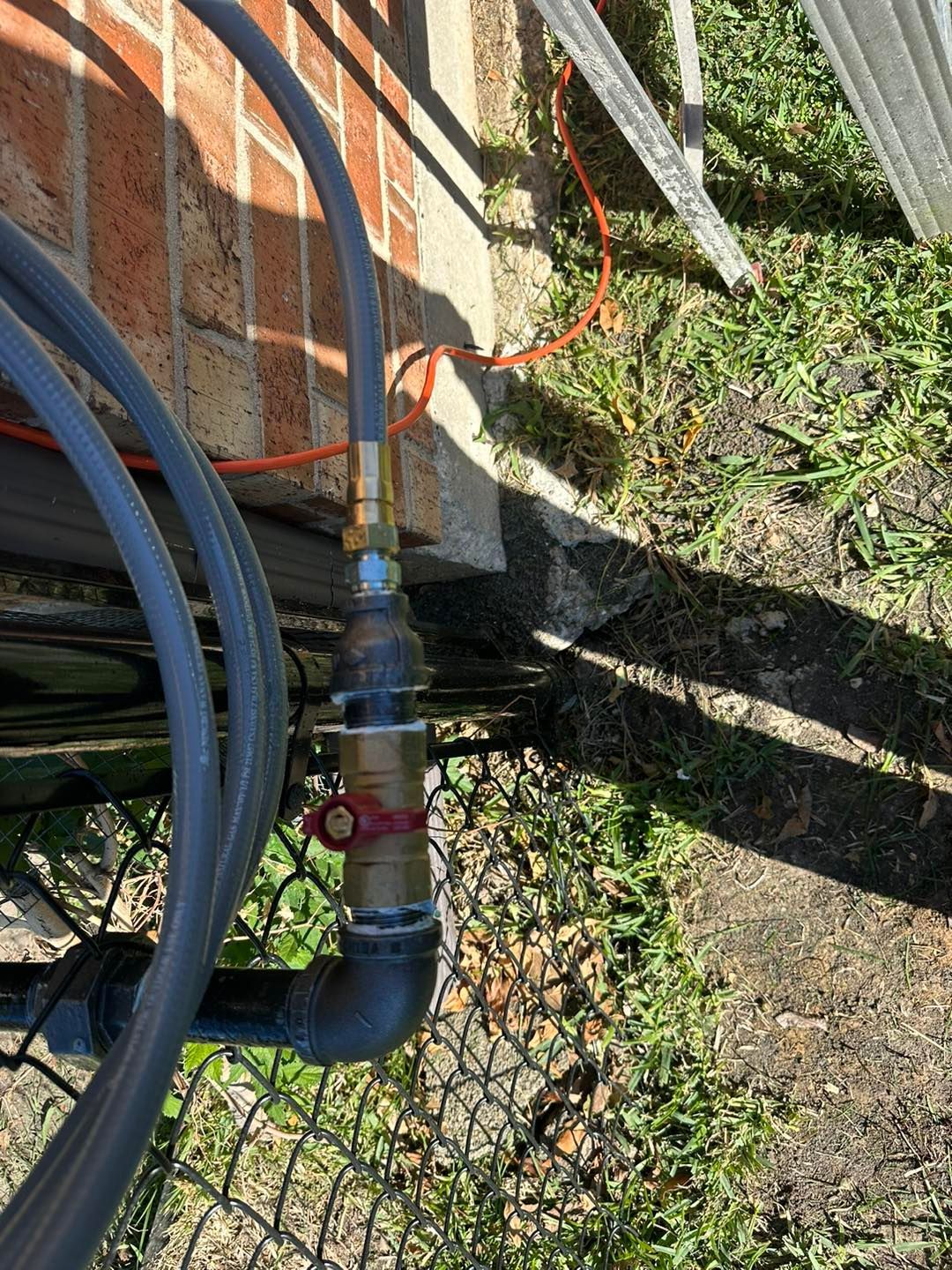 Garden irrigation hose and metal pipe with valve beside a brick wall and grassy ground.