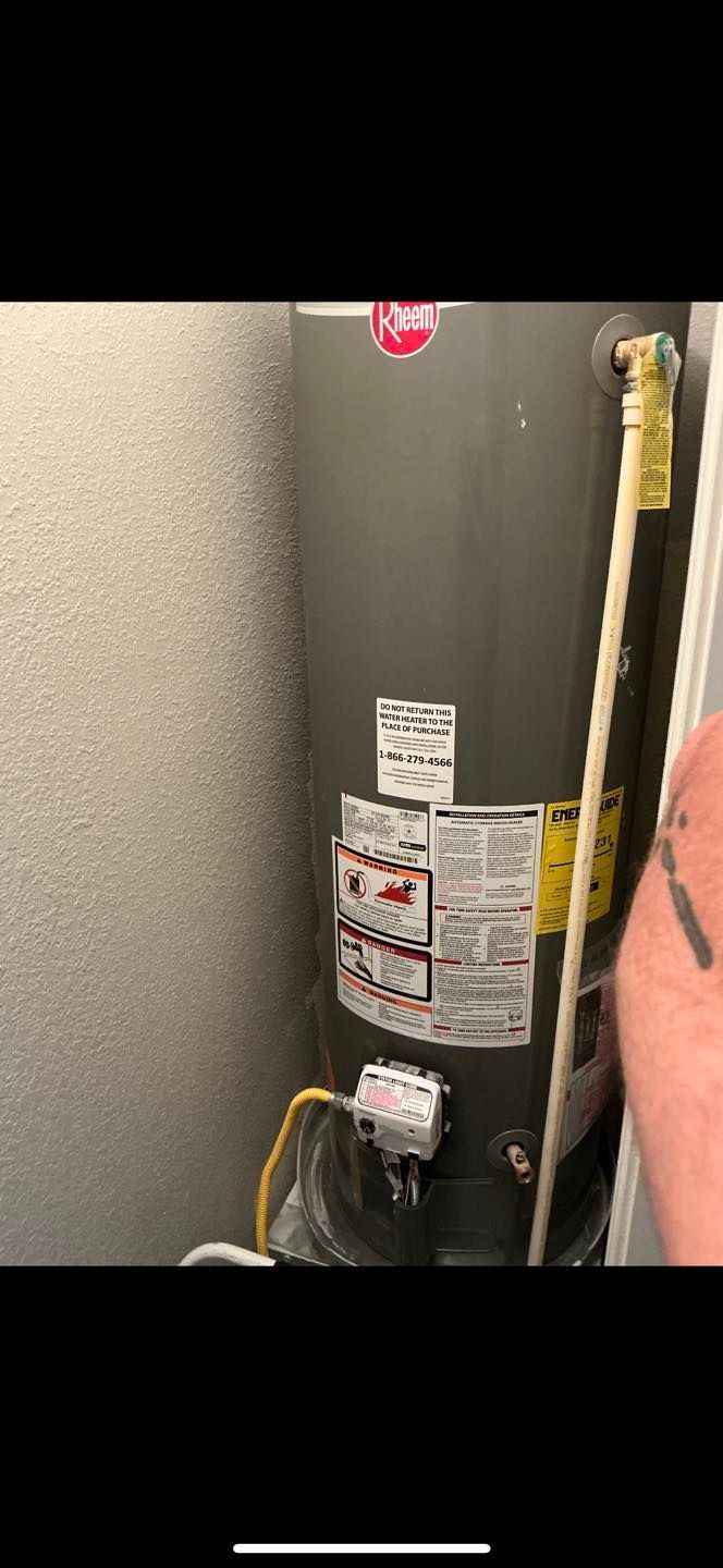 Close-up of a gray water heater with warning labels and a yellow pipe in a utility closet