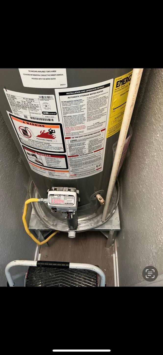 Water heater with warning labels, wiring, and a small component on a utility room wall.
