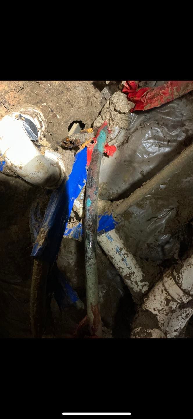 Dark close-up of a muddy cave or tunnel with blue and red painted markings on rock and a rope or cable.