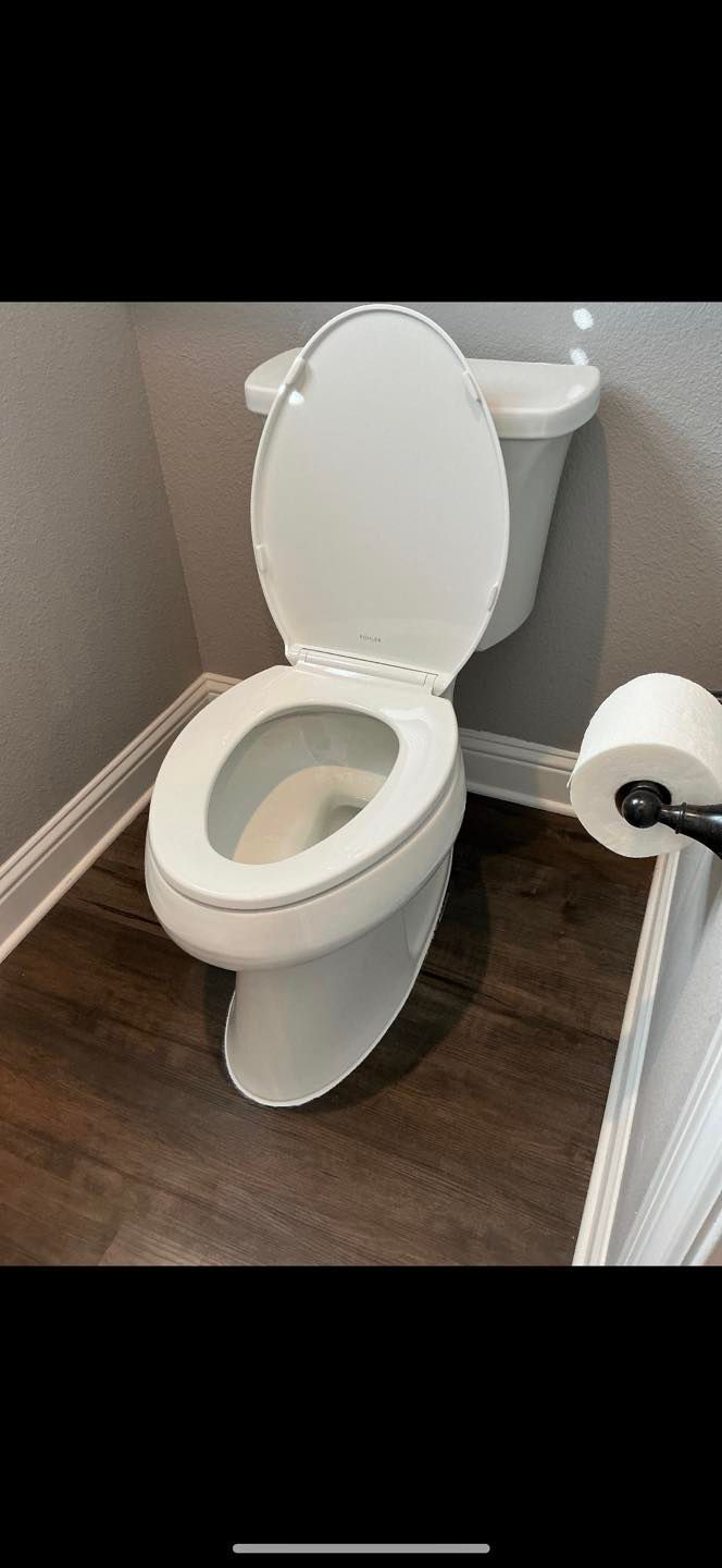 White toilet with seat up in a small bathroom with wood-look floor.