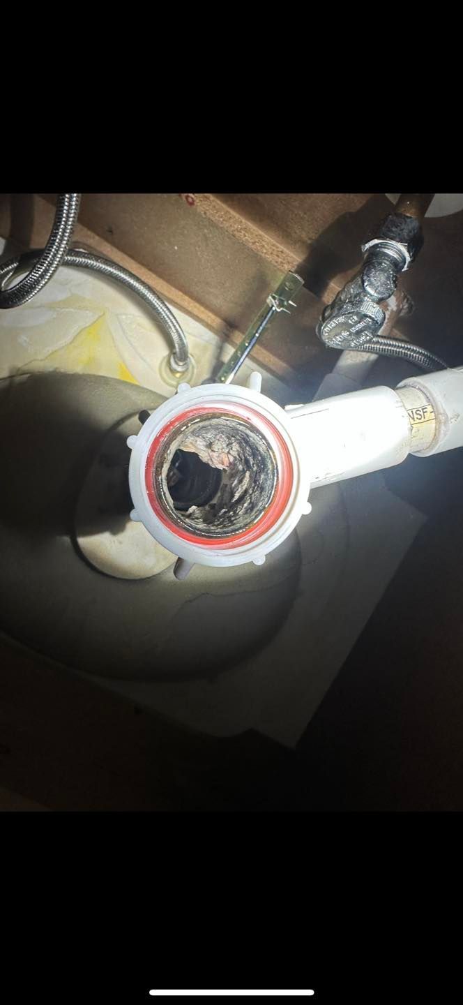 Close-up of a white pipe fitting with a red-ringed opening and surrounding hoses under a sink.