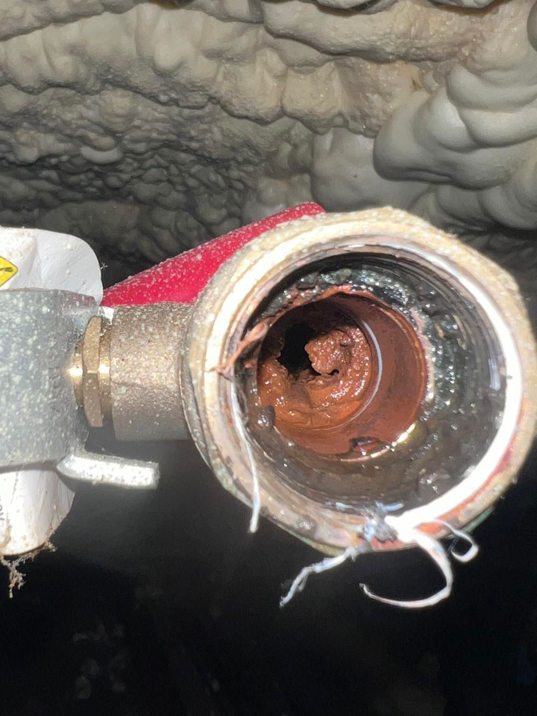 Rust-clogged pipe opening with corrosion inside, shown in a cramped wall cavity