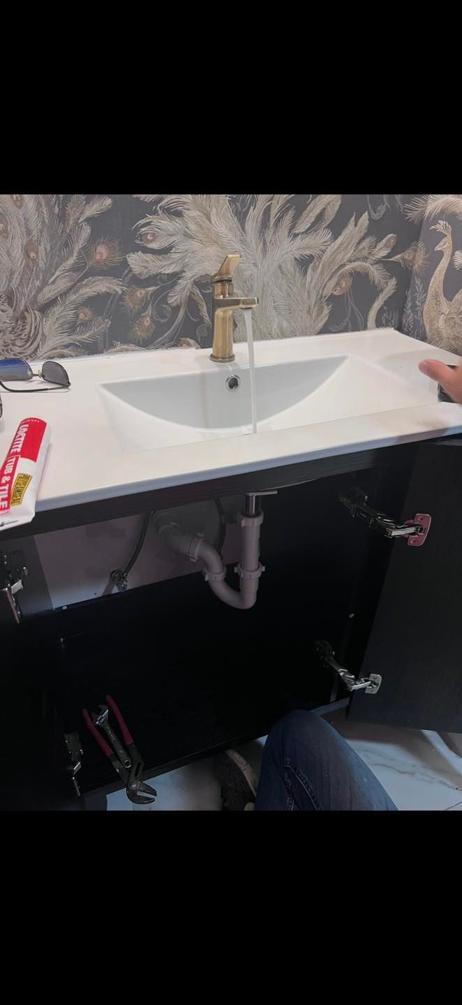 Modern bathroom sink with gold faucet, white countertop, and dark vanity against patterned wallpaper