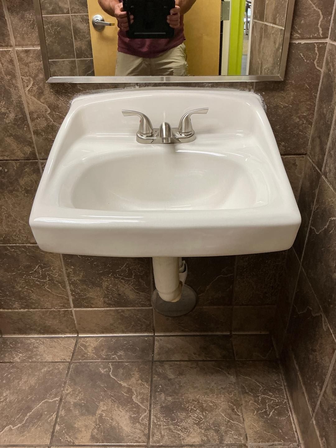 White wall-mounted sink with chrome faucet in a brown-tiled bathroom, seen below a mirror