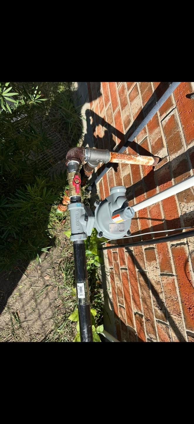 Three outdoor water meters on a brick wall beside a black metal fence and greenery.