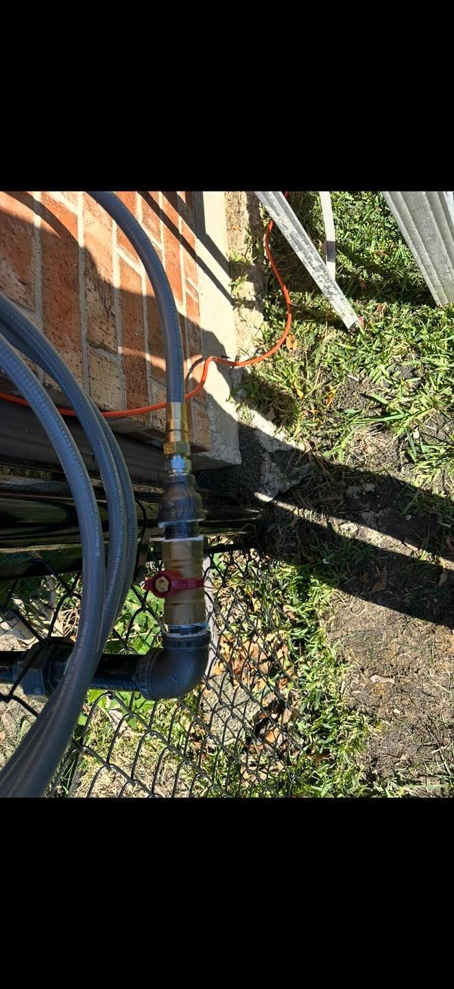 Close-up of garden hoses connected to a brick wall near a concrete edge and grassy ground