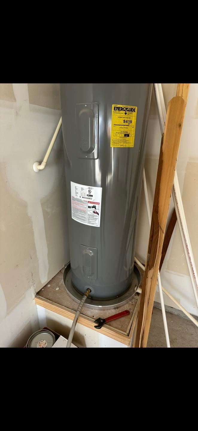 Gray water heater in a utility closet with warning labels and exposed pipes.