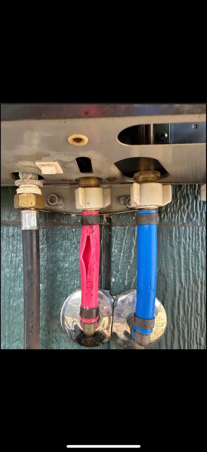 Close-up of plumbing under a sink, showing red and blue water supply lines and metal fittings.