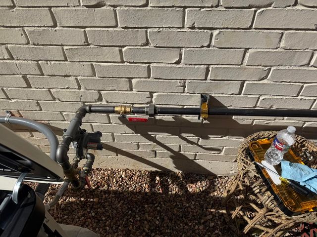 Irrigation pipes and a faucet against a brick wall, with a small basket of items on the right.