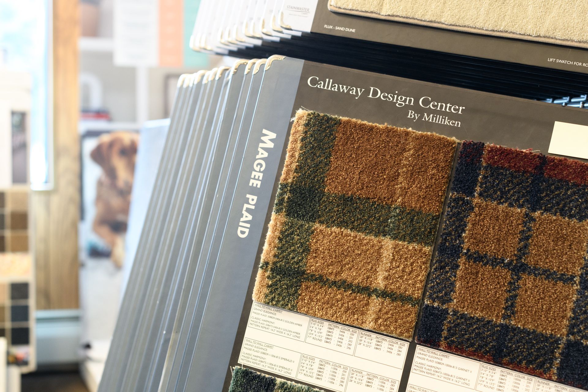 A stack of carpet samples in a store with a dog in the background.