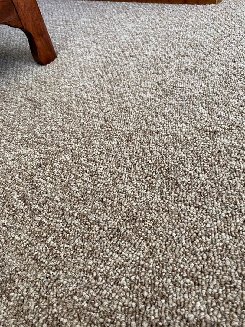 A close up of a carpeted floor with a chair in the background.