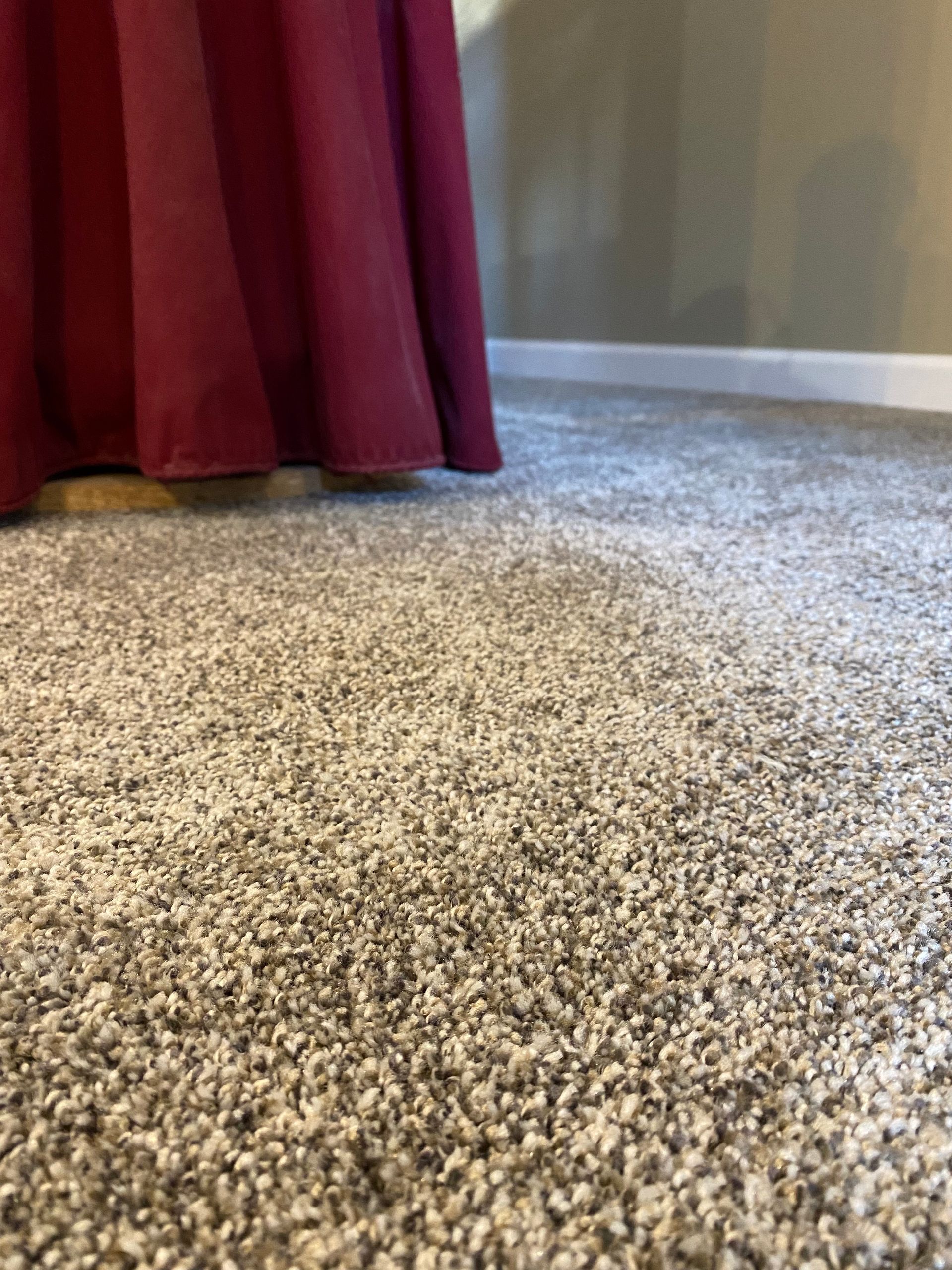 A close up of a carpeted floor with a red curtain in the background.