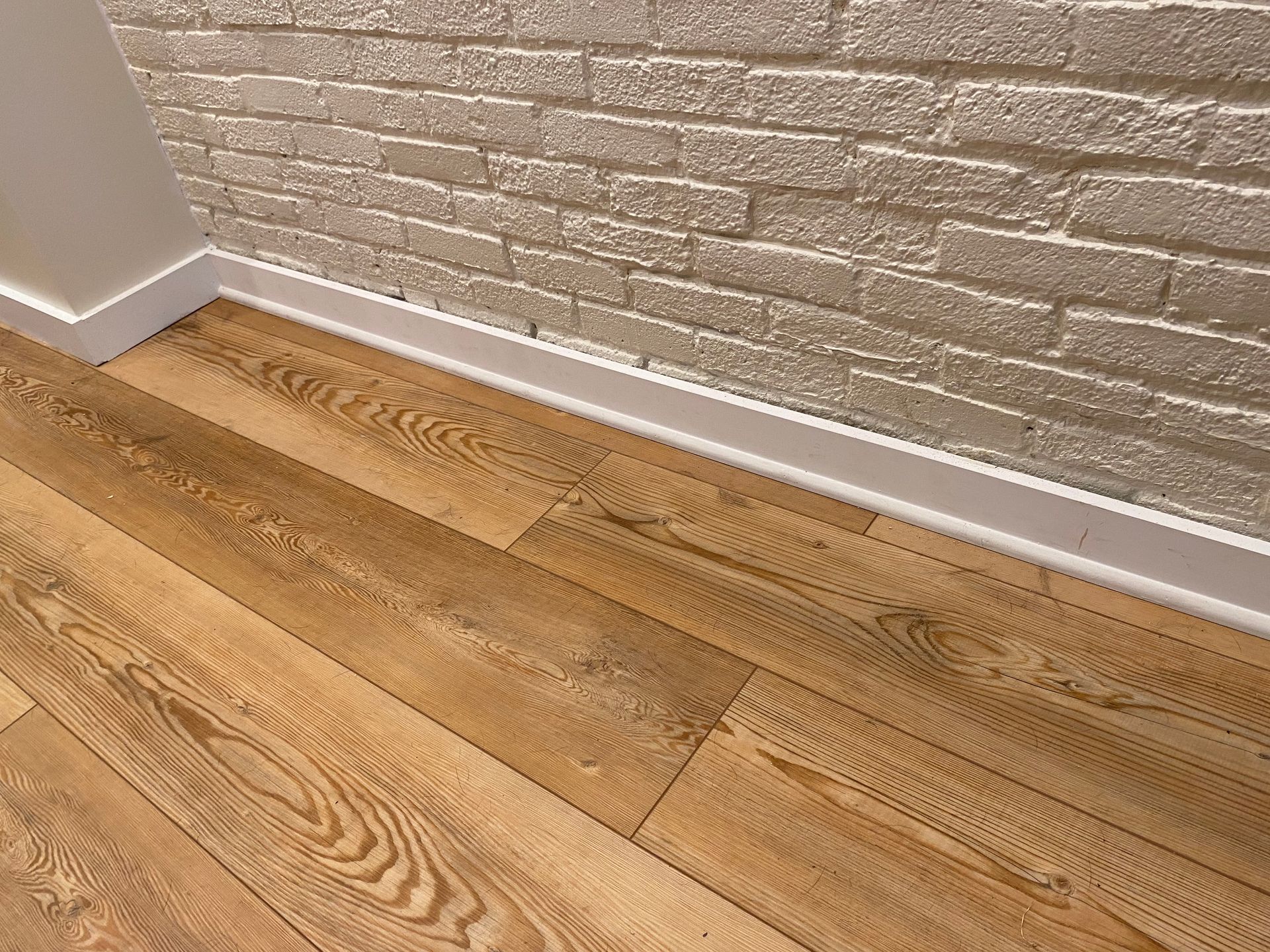 A close up of a wooden floor in front of a brick wall.