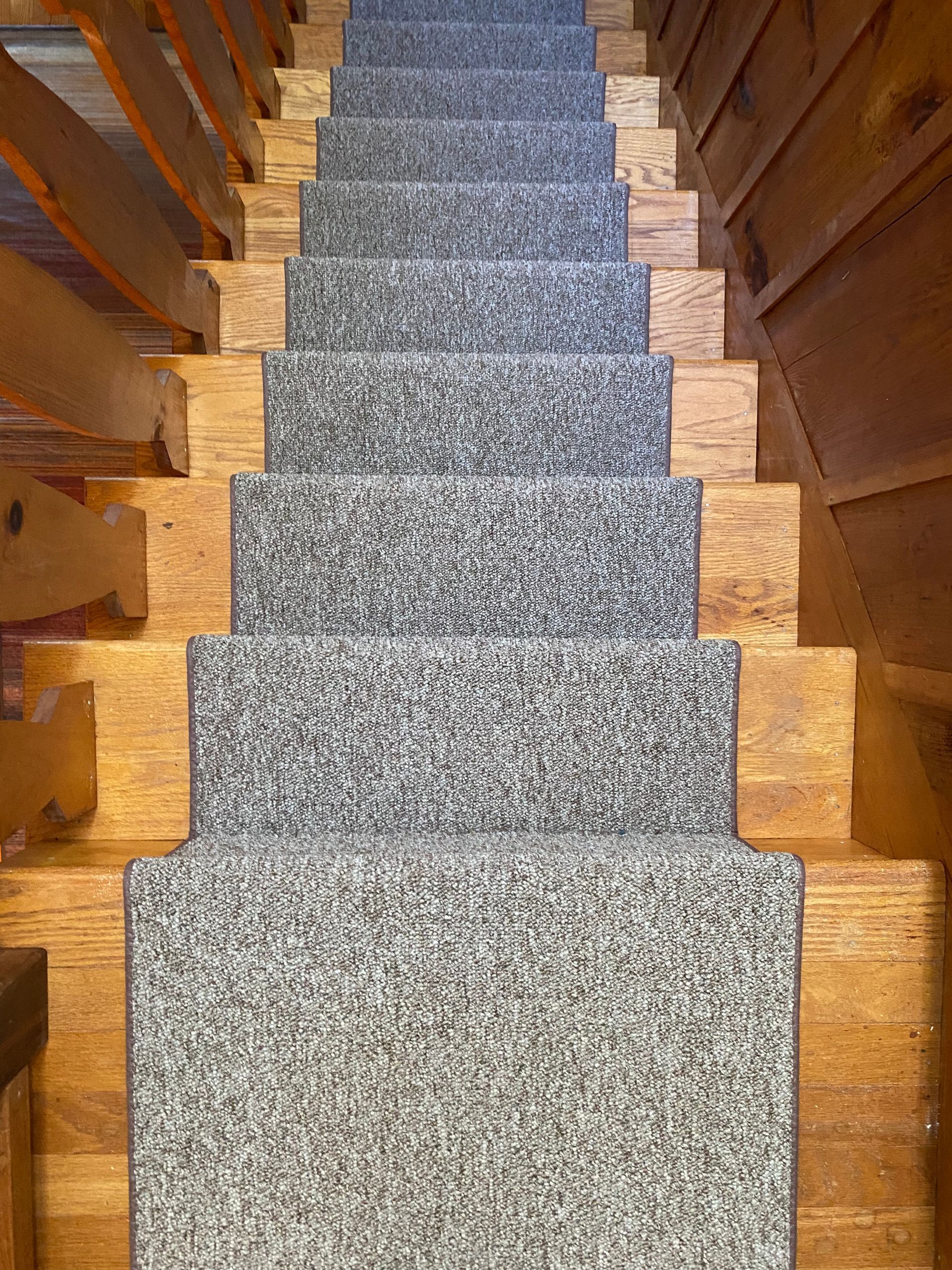 A wooden staircase with a gray carpet on the steps.