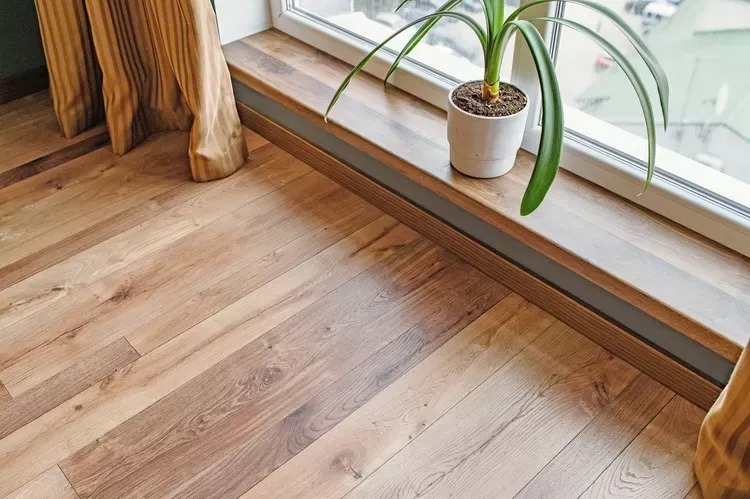 A potted plant is sitting on a window sill next to a wooden floor.