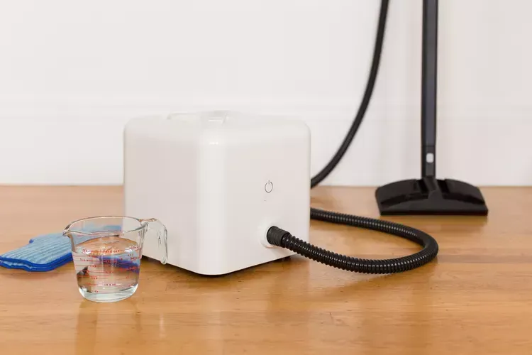 A mop steamer is sitting on a wooden table next to a measuring cup of water. A mop steamer is sitting on a wooden table next to a measuring cup of water.