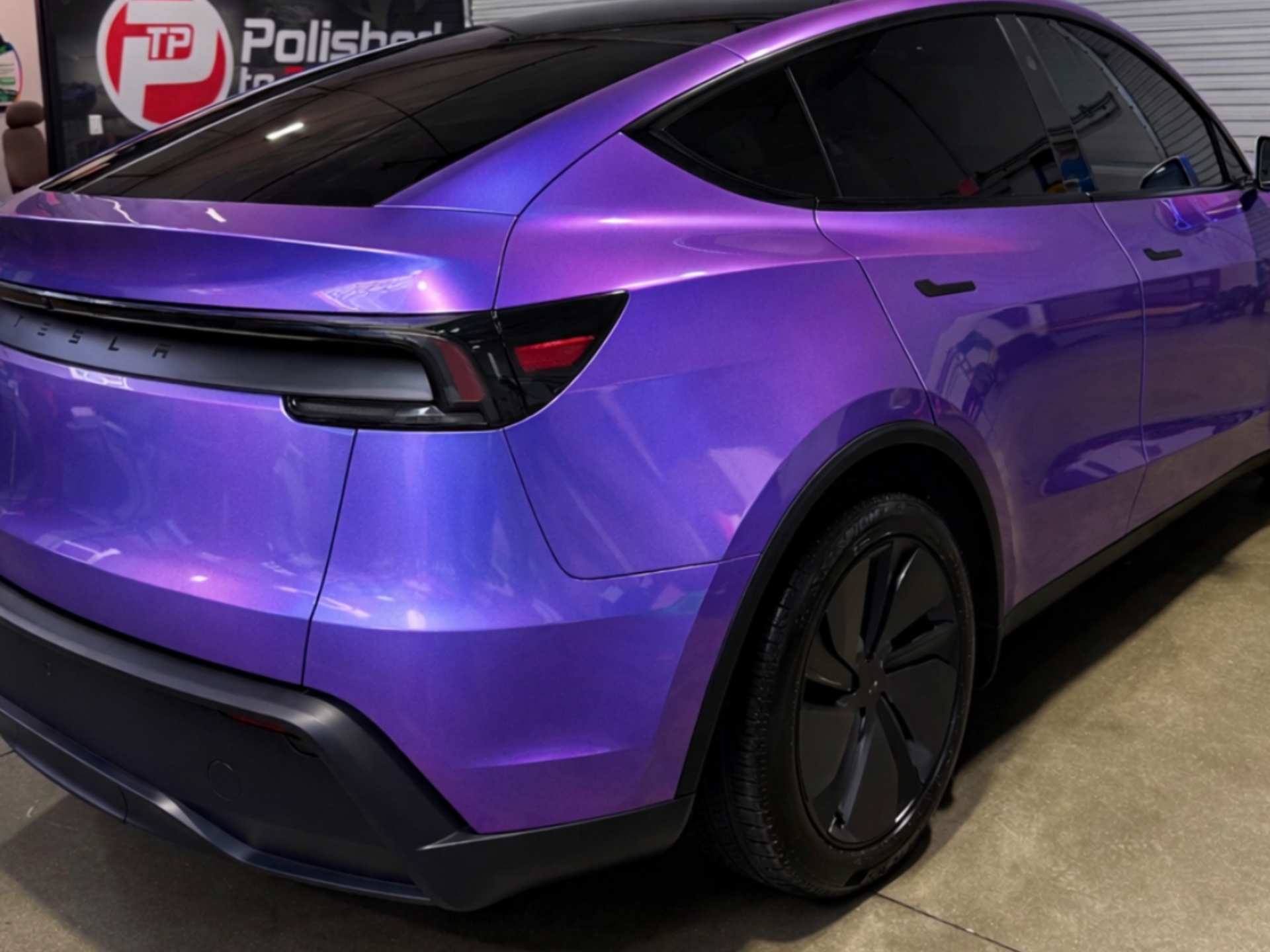 A purple, color-shifting Tesla Model Y parked inside a garage with a logo on the back wall.