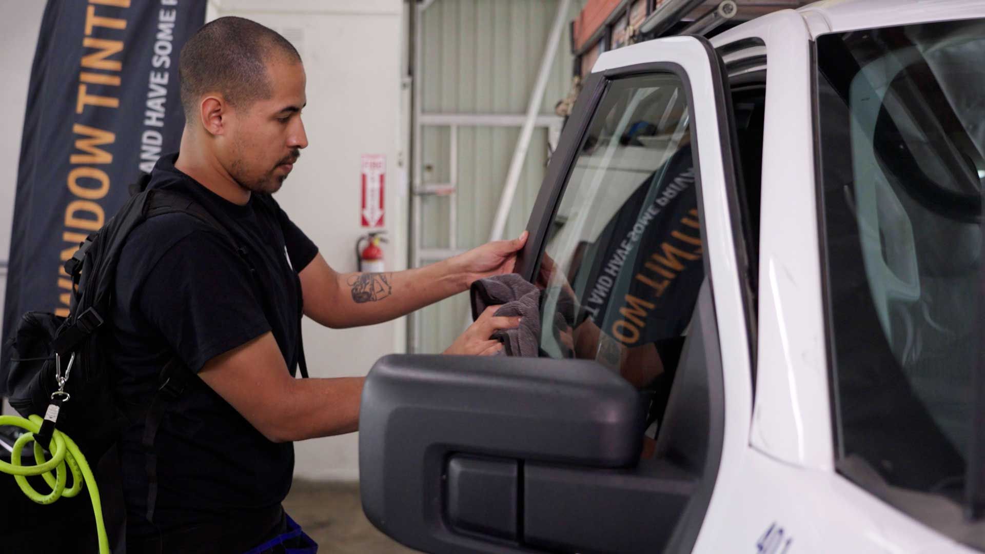 A professional wipes down the interior glass of a white truck door at a window tinting shop.