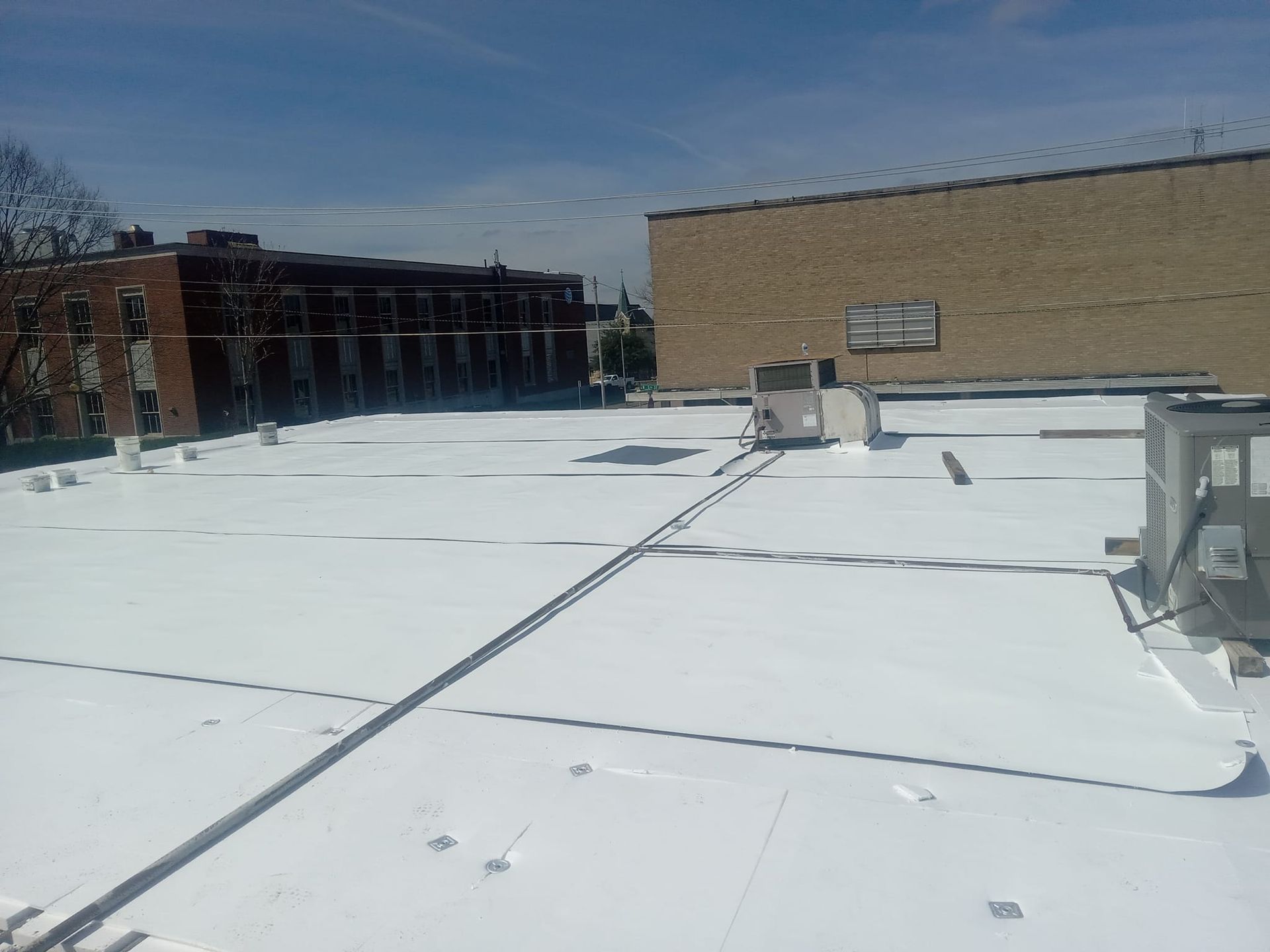 The roof of a building with a white roof and a brown building in the background.