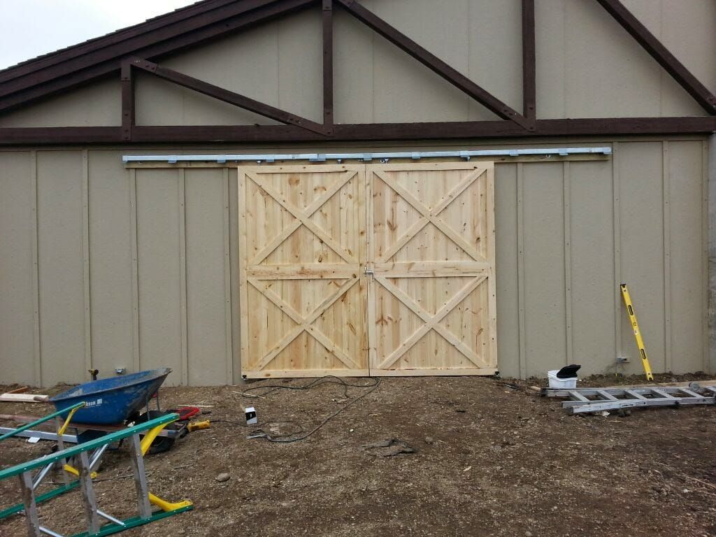 A wooden barn door is being installed on the side of a building.