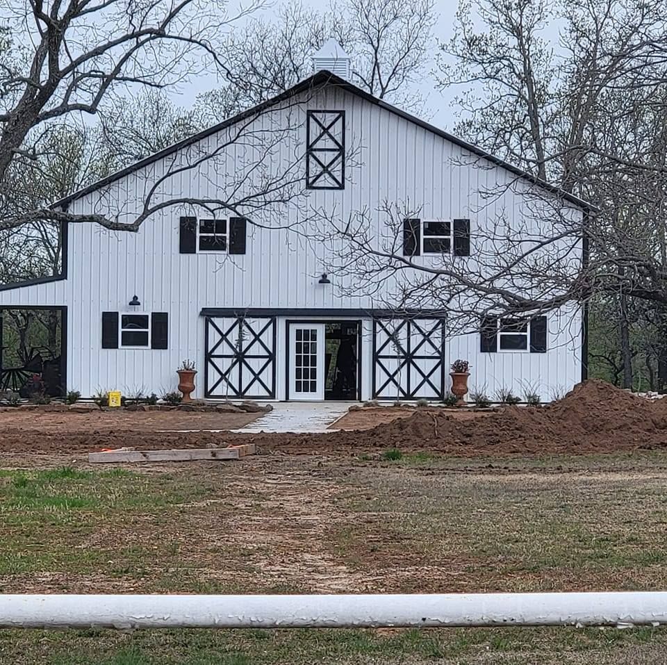 A white barn with black shutters is sitting in the middle of a grassy field.