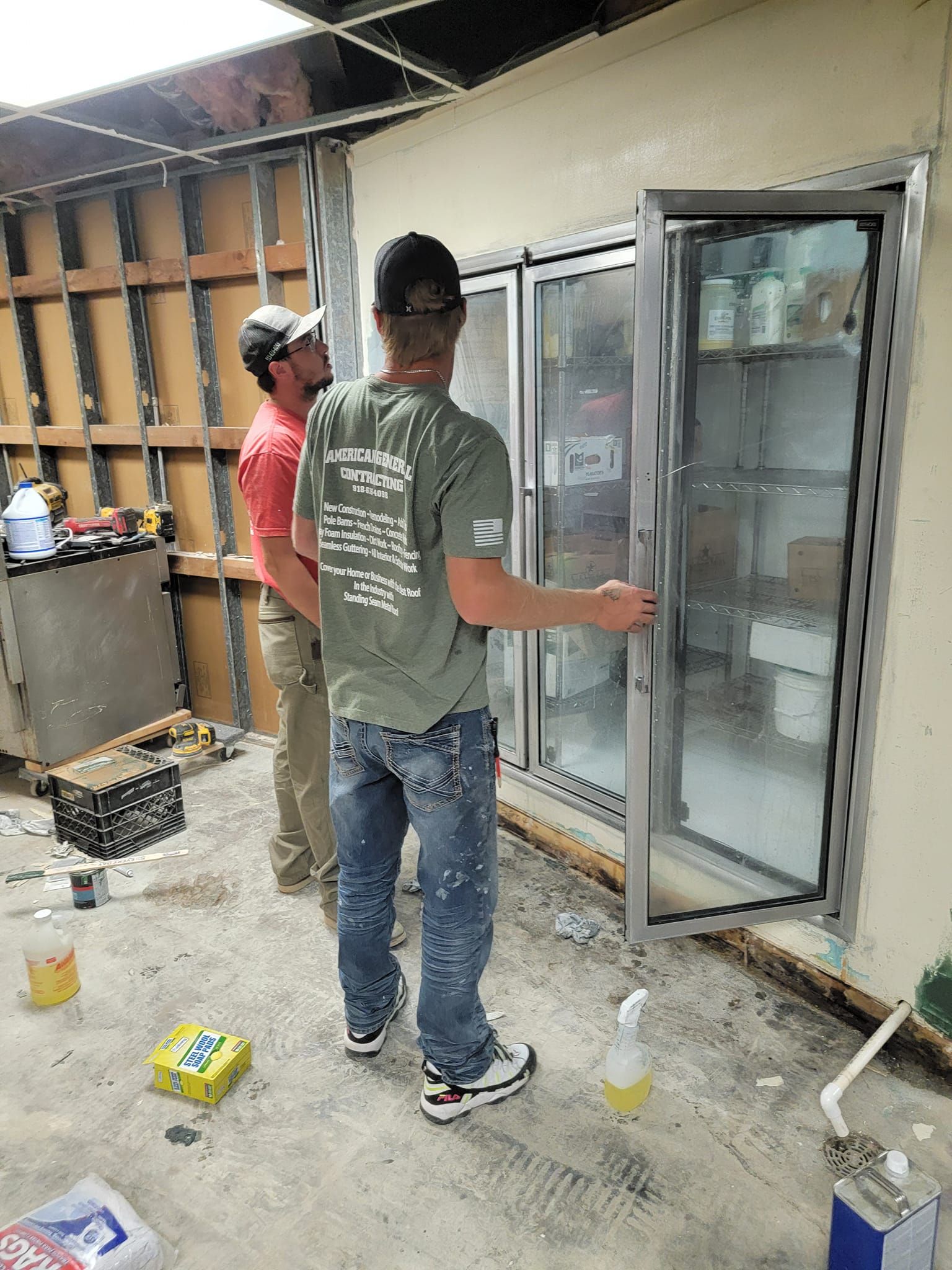 Two men are working on a refrigerator in a room.