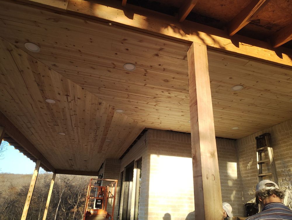 Wooden porch ceiling under construction; a post, lights, and workers are visible.
