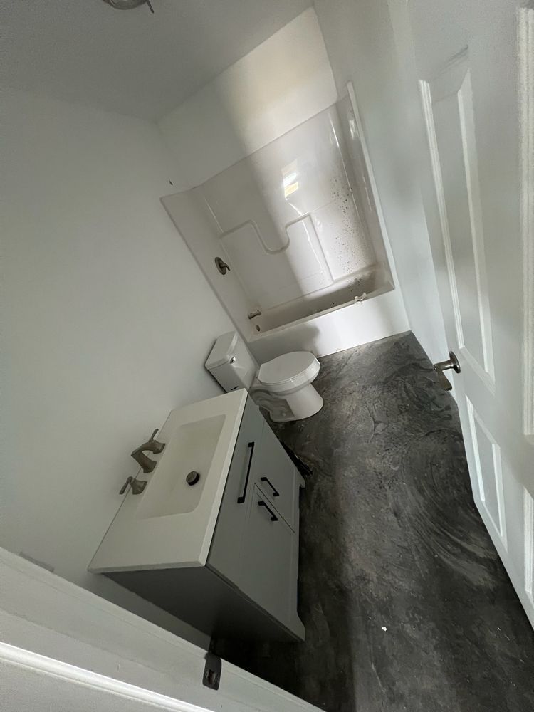 Bathroom with white walls, gray vanity, white tub, and black flooring.
