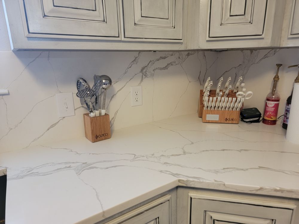 White countertop with gray veining, kitchen utensils, and cabinets.