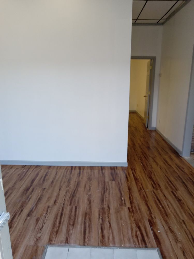 Empty room with wood-look flooring and white walls, hallway visible, doorway.