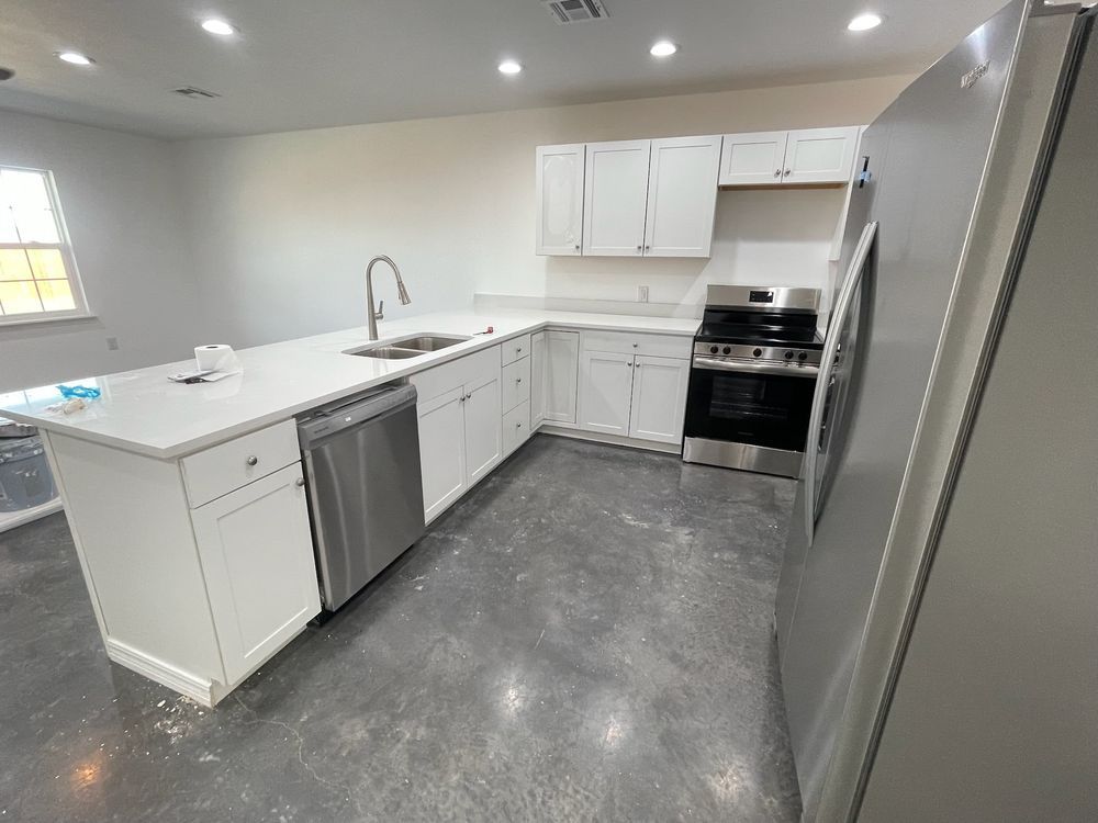 Modern white kitchen with island, stainless steel appliances, and gray concrete floor.