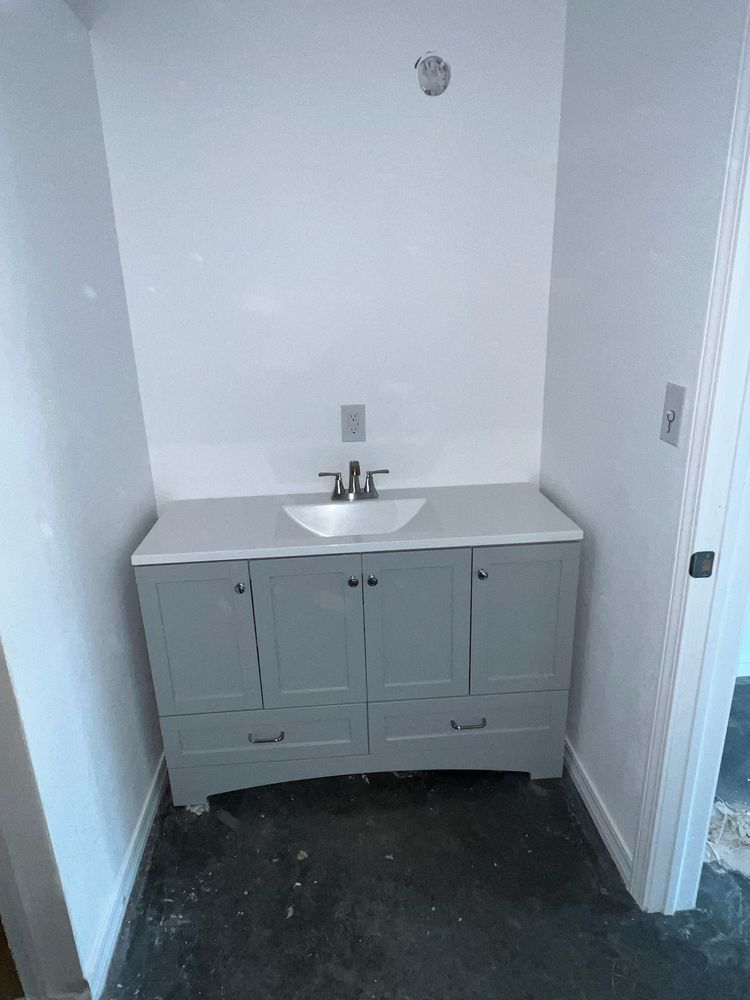 Gray bathroom vanity with white countertop and sink against a white wall, in a narrow alcove.