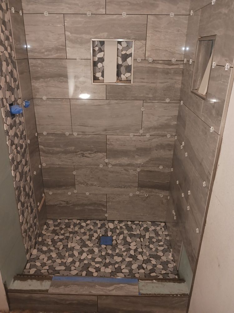 Shower under construction; gray and patterned tiles on walls and floor.
