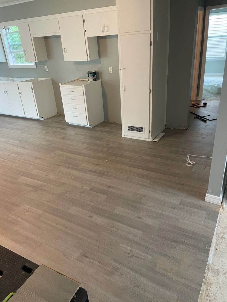 Kitchen with new light-colored wood-look flooring and white cabinets, some still being installed.