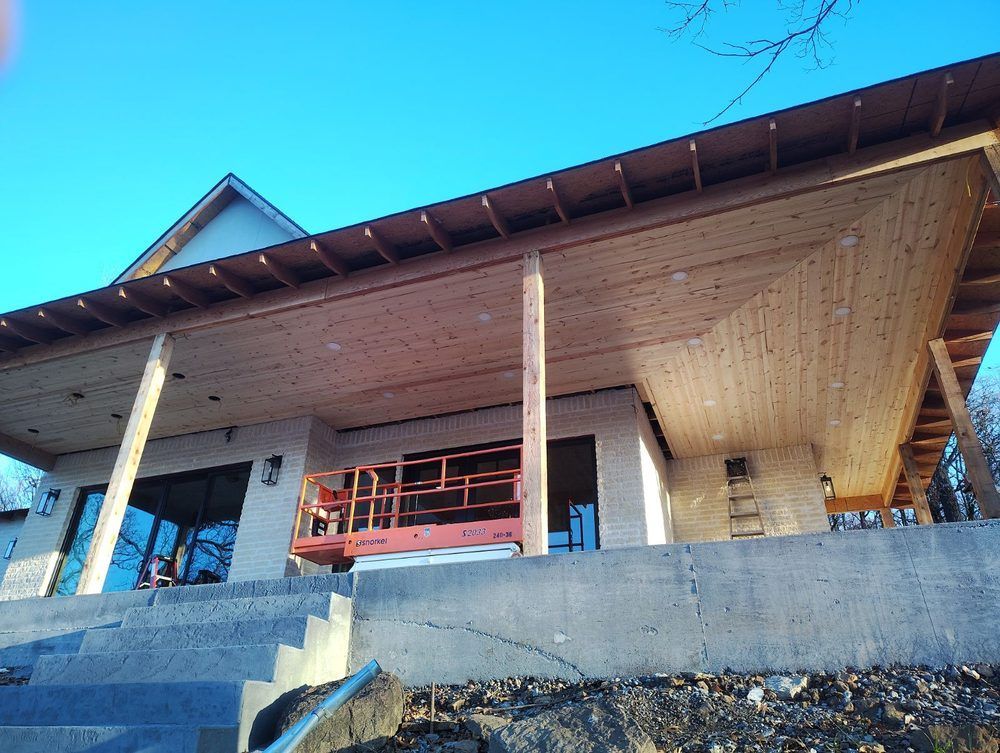 A partially constructed modern home with a wooden overhang and concrete base under a blue sky.